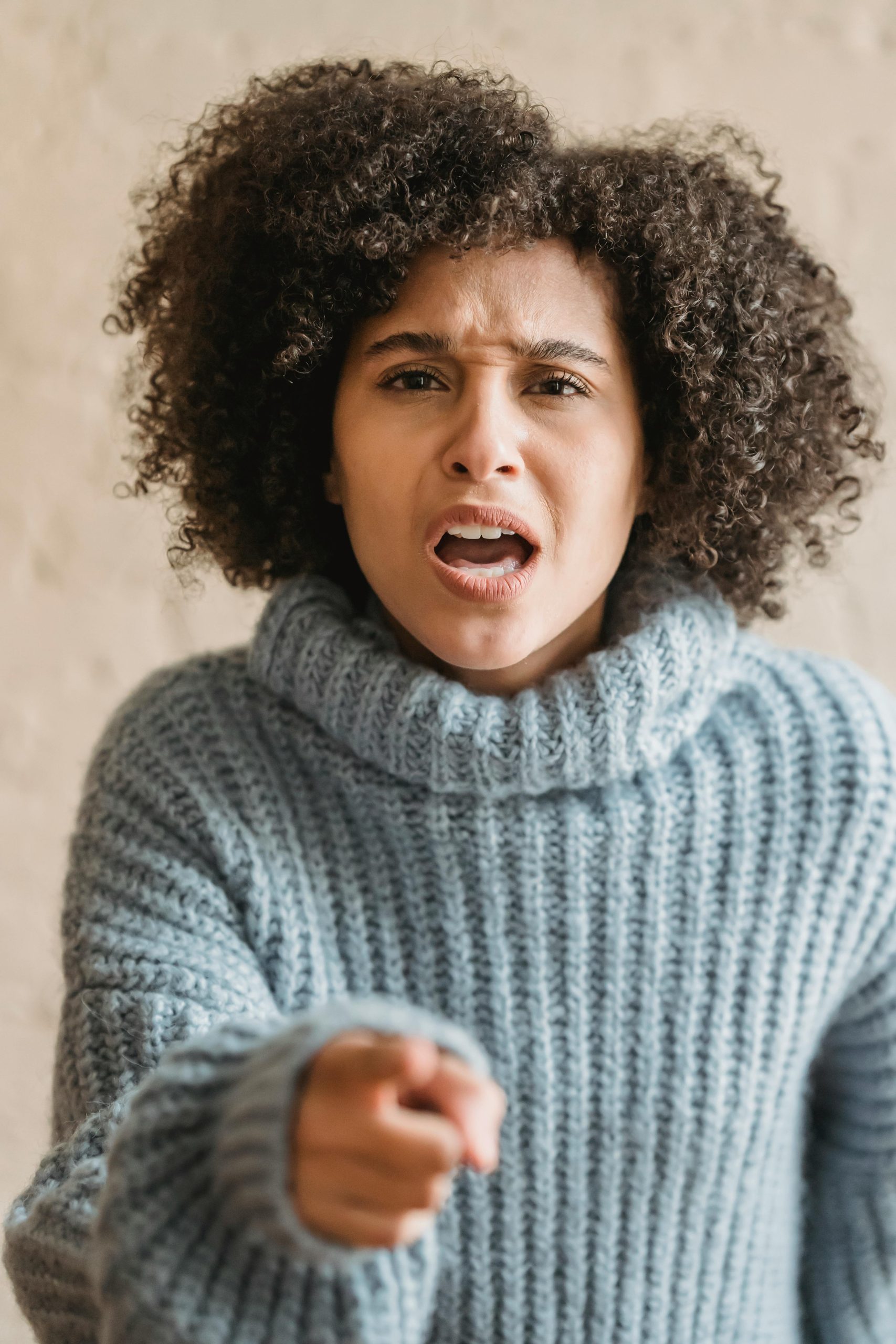 An expressive woman in a cozy sweater pointing and shouting indoors.
