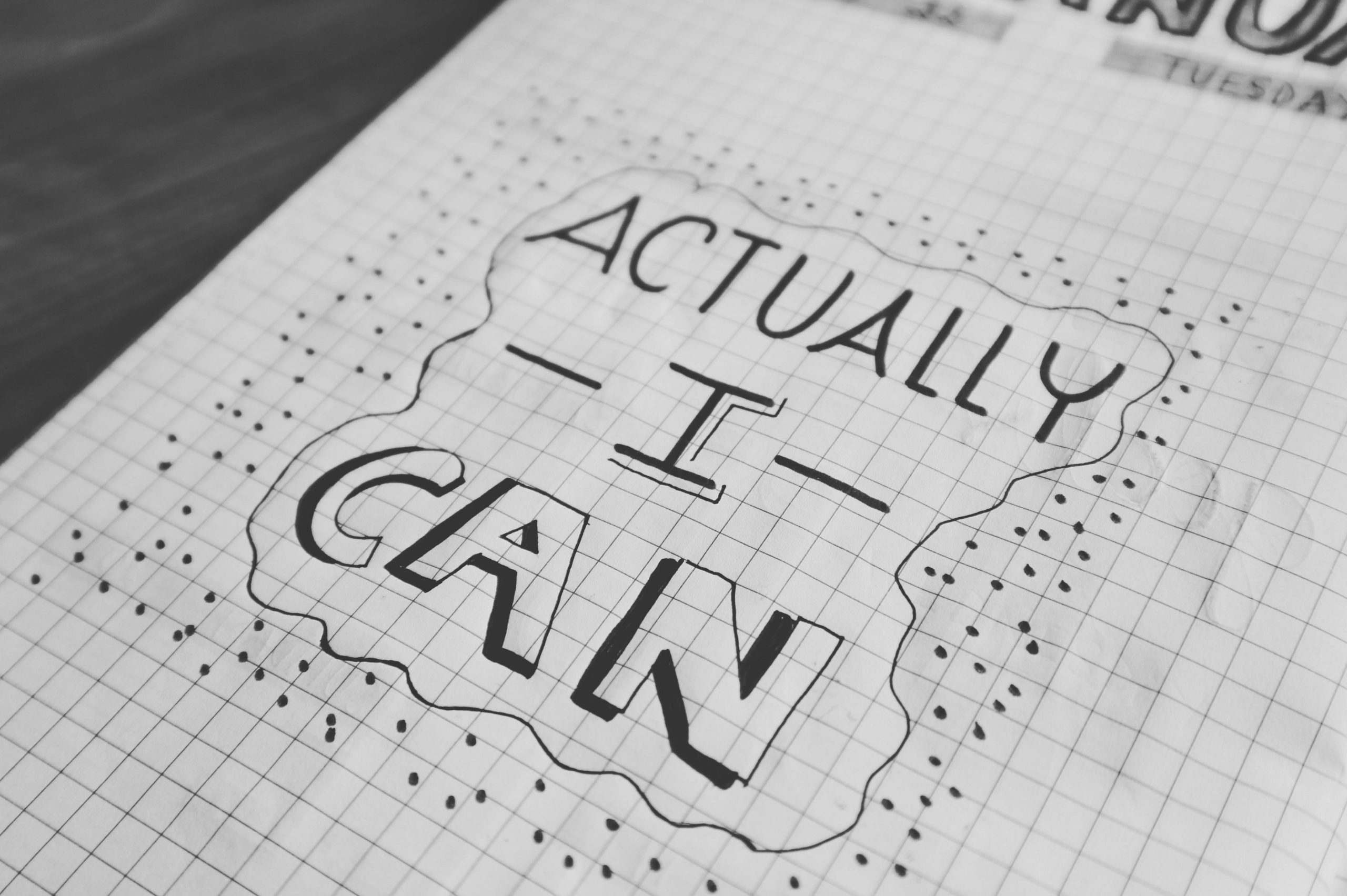 Motivational text 'Actually I Can' on a grid paper background. Black and white close-up.