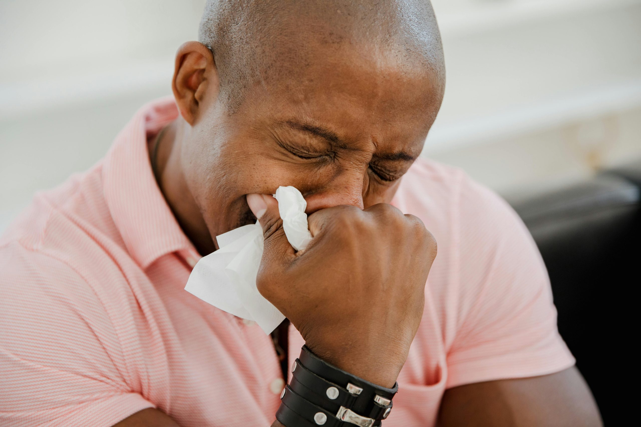 A close-up image of a black man in a pink shirt expressing strong emotions.