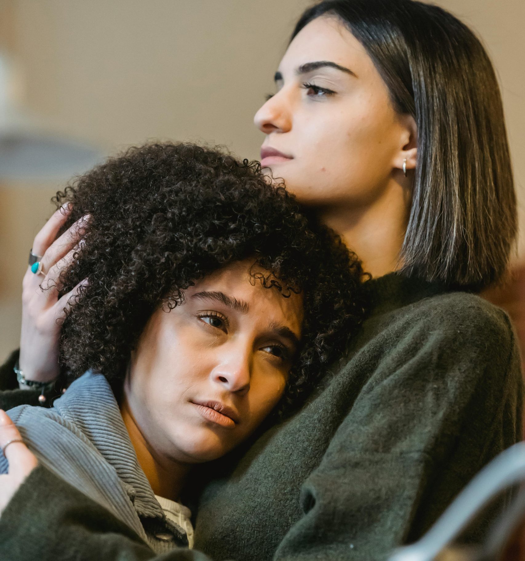 Caring female cuddling and stroking head of unhappy African American best friend while standing close and looking away